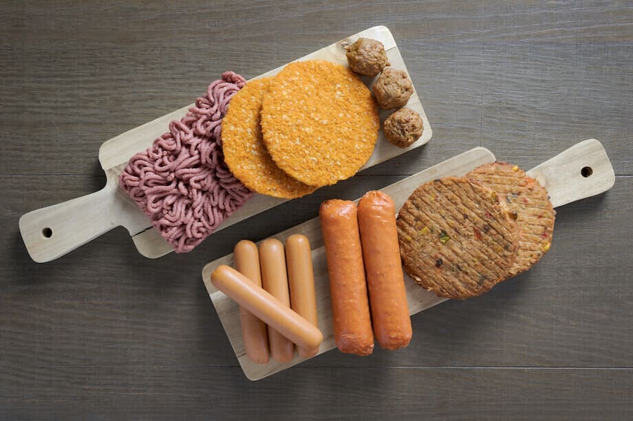 Plant based burgers, hot dogs, and other meats on wooden paddles