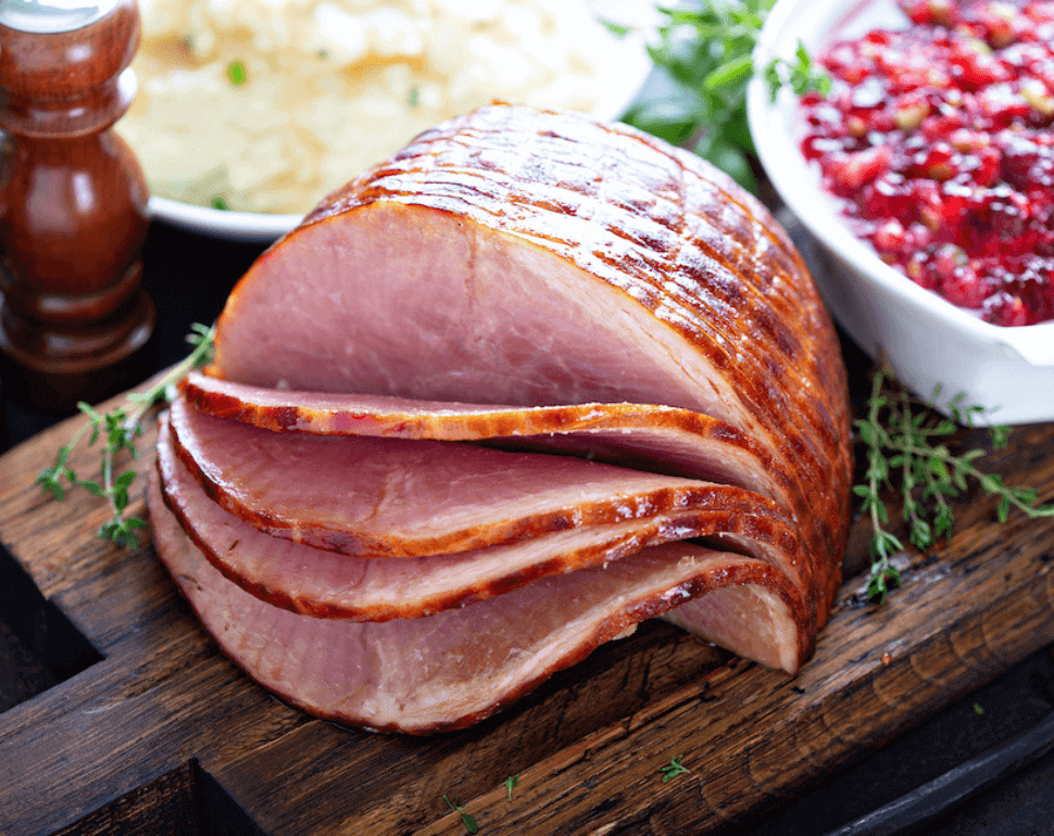 Honey glazed ham sliced next to mashed potatoes and cranberries