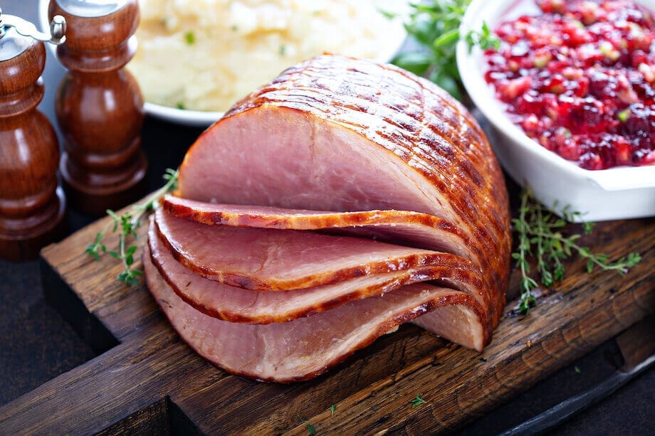 Honey glazed ham sliced next to mashed potatoes and cranberries